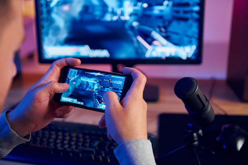 Using the smartphone. Online streamer playing FPS shooter game at home